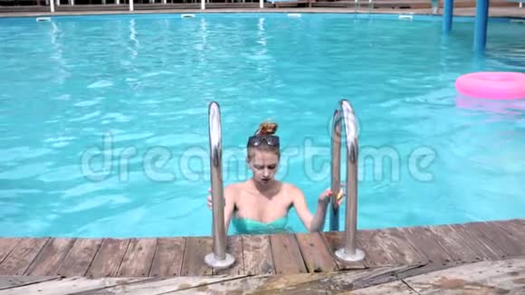 年轻的女人从游泳池出来穿着绿松石泳衣的漂亮女孩在泳池边休息苗条的女人穿着比基尼视频的预览图