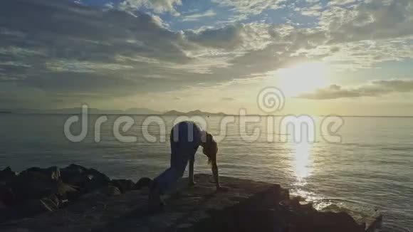FlycamViewGirl在海洋日出时在岩石上做瑜伽视频的预览图