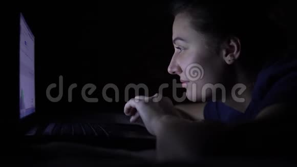 一个迷人的年轻女孩在晚上躺在床上时使用移动电脑孤立光视频的预览图