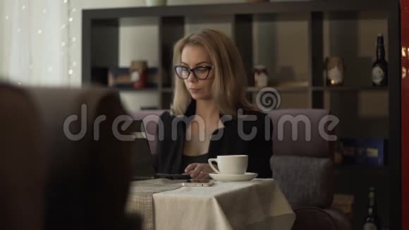 年轻的女商人戴着眼镜在咖啡馆的沙发上敲着键盘视频的预览图