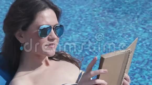 在海滩上戴太阳镜看书的漂亮女性休闲视频的预览图