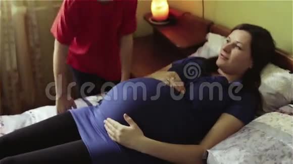 小男孩把耳朵贴在怀孕母亲的大肚子上视频的预览图
