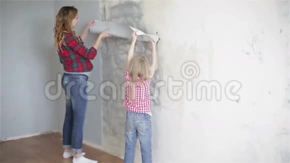 母亲和女儿穿着格子衬衫正试着在墙上贴一张新墙纸视频的预览图