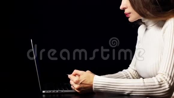 美丽的黑发女人用她的信用卡用笔记本电脑在线支付黑色背景暖色空间视频的预览图