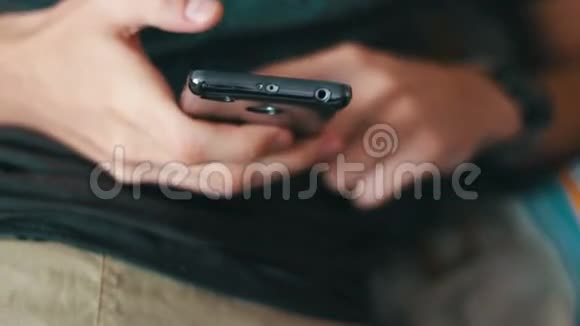 穿T恤和短裤的男人躺在沙发上手里拿着一部智能手机视频的预览图