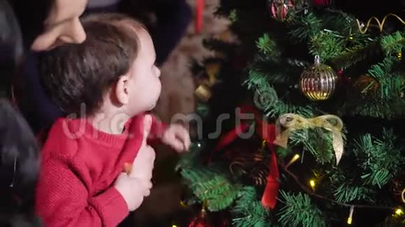 年轻的母亲抱着他的胳膊她的小男孩帮助一个孩子打扮圣诞树男孩抓住针视频的预览图