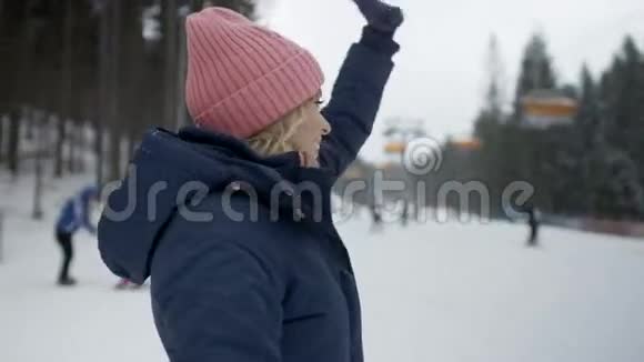 一位穿着冬装的年轻微笑女子在滑雪电梯附近向她的朋友挥手的肖像视频的预览图