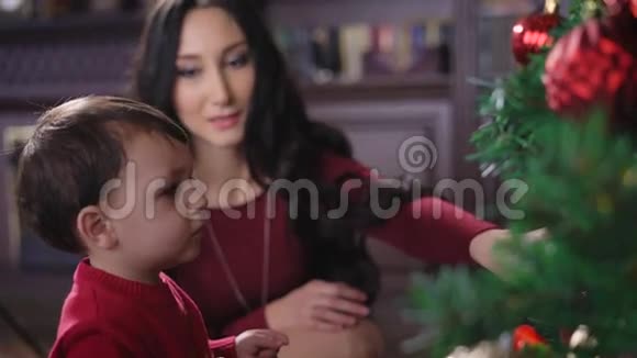 一个女孩带着一个孩子在家圣诞树布鲁内特看着孩子微笑着孩子和一个视频的预览图
