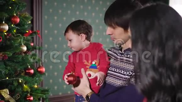 年轻的母亲留着长长的黑发穿着一件漂亮的衣服让你的小儿子装饰一棵华丽的圣诞树爸爸视频的预览图