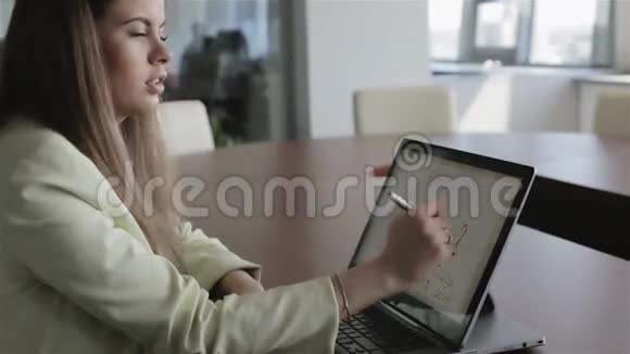 一个穿黄色夹克的女商人正用手写笔在笔记本电脑屏幕上绘制利润图视频的预览图