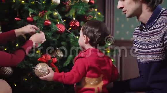 一个年轻的家庭正在家里准备圣诞节长发黑发女人装饰圣诞树孩子视频的预览图