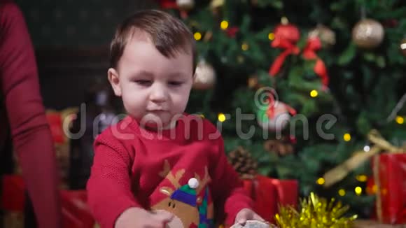 一个黑头发的小男孩穿着一件红色的毛衣鹿在玩黄色闪闪发光的圣诞花环他敲她一下视频的预览图