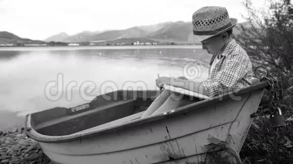 一个男孩坐在渔船上看书的黑白视频视频的预览图