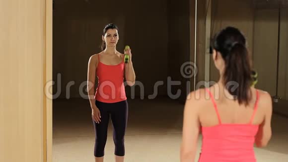 运动的女人用哑铃抬高肌肉健身模特照镜子视频的预览图