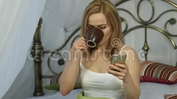 快乐的女人坐在床上跳舞唱歌喝咖啡和朋友在电话里聊天4K视频的预览图
