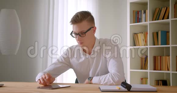 年轻英俊的白种人商人戴着眼镜在办公室里用平板电脑拍摄的特写照片视频的预览图