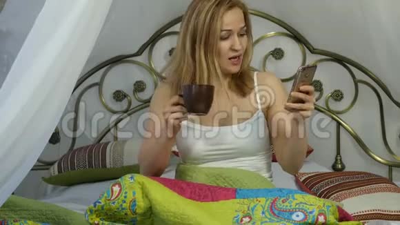 快乐的女人坐在床上跳舞唱歌喝咖啡和朋友在电话里聊天4K视频的预览图