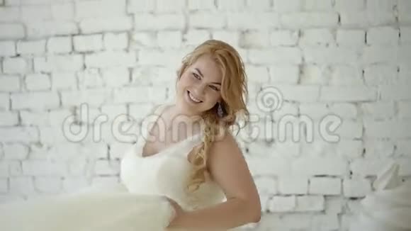 可爱的金发女郎穿着婚纱在后台巨大的冰淇淋和通心粉的工作室里摆姿势跳舞视频的预览图