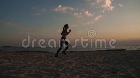 20岁的女孩在日落时在沙滩上奔跑在户外慢跑慢动作视频的预览图