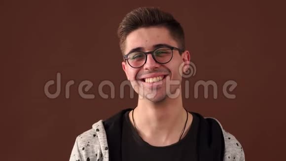 棕色背景下戴眼镜的快乐笑年轻人的肖像视频的预览图