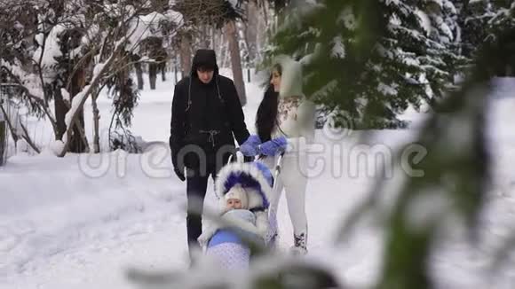 一对夫妇带着一个孩子走过雪地公园的慢动作视频穿黑色夹克深蓝色裤子的男人视频的预览图