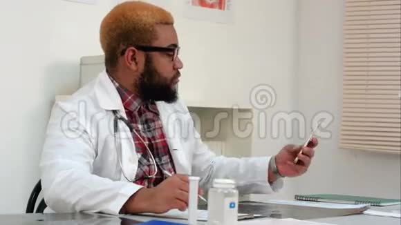非裔美国男性医务工作者在办公桌上接电话视频的预览图