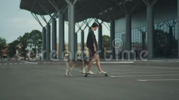 年轻漂亮的女人带着她的哈士奇狗骑在滑板或长板上视频的预览图