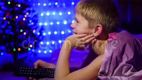 孩子看着躺在床上的电视背景中圣诞杉木的灯光和花环视频的预览图