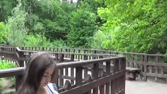 年轻迷人的女孩在长凳上用手机夏日公园微笑高清拍摄移动摄像机全景视频的预览图