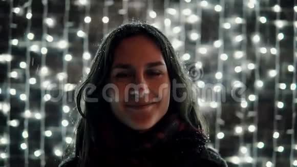年轻漂亮的女人在装饰墙前的圣诞夜里享受着降雪满是闪闪发光的灯光视频的预览图