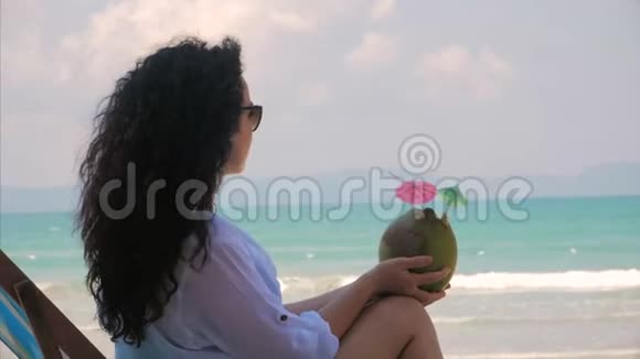一个欧洲美丽的可爱的布鲁内特年轻女人或一个快乐的女孩的肖像在阳光下喝椰子在风中喝一杯视频的预览图