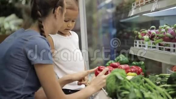 年轻的母亲教她的小女儿选择超市里的蔬菜视频的预览图