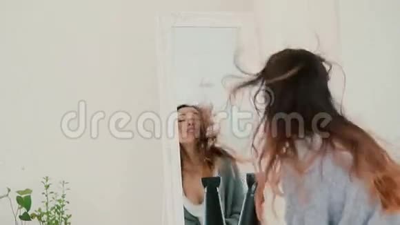 幸福的年轻女子在卧室里唱歌看着镜子女孩用吹风机作为麦克风慢动作视频的预览图