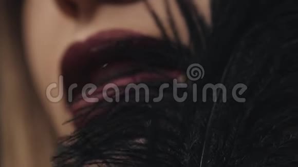 女性面部特写模特护肤化妆品装饰化妆品轻轻触摸脸颊上的黑色羽毛眼睛马斯卡视频的预览图