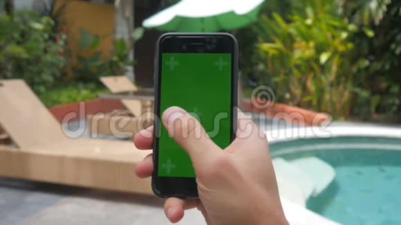 在泳池背景下度假时男性手触摸智能手机的特写绿色屏幕Chroma键视频的预览图