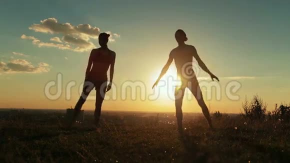 日落时分在公园里摆三角造型的运动男女剪影视频的预览图
