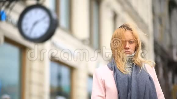 一个穿着粉红色外套和毛衣的女人站在时钟附近拥挤的街道中间等待着视频的预览图