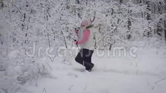 踩着脚的女人在森林里用滑雪杆穿过雪堆女运动员正在做北欧运动视频的预览图