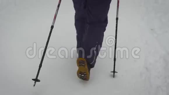 一个穿着温暖的黑色裤子和带着滑雪杆在森林里行走的沉重靴子的女人的踩腿女性视频的预览图