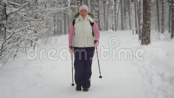 活跃的女人穿着温暖的衣服在森林里做北欧行走快乐的女运动员踩着滑雪杆视频的预览图