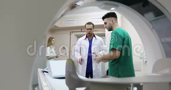 4两位穿着医疗服的年轻医生在一家诊所的橱柜CT扫描仪里交谈视频的预览图