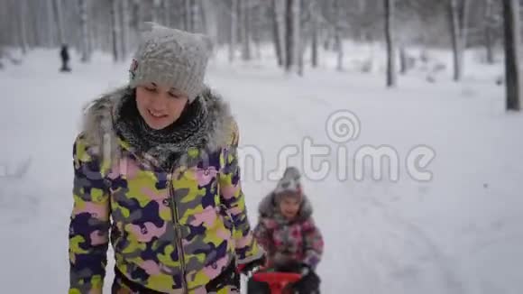 母亲骑着一个小女孩在公园的雪道上雪橇可爱的女人积极地与她共度闲暇时光视频的预览图