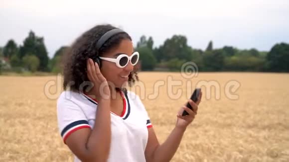非洲裔美国少女戴着白色太阳镜走着听无线耳机音乐的年轻女子视频的预览图