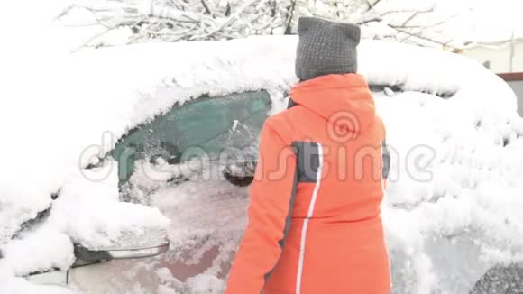 一位年轻女子在大雪纷飞后在汽车挡风玻璃上擦雪擦冰视频的预览图