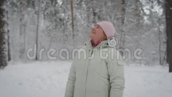 幸福的女人穿着米色外套和粉红色的帽子站在森林里抬头微笑退休的老年女性视频的预览图