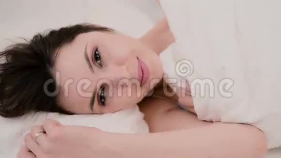 年轻迷人的女人躺在床上女孩看着相机微笑光房快乐的女人视频的预览图