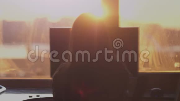 在美丽的夕阳下年轻的商务女性坐在窗边的一张桌子上在电脑上工作慢动作视频的预览图