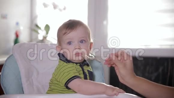 好奇可爱的宝宝环顾四周坐在婴儿椅上妈妈用勺子喂她可爱的一岁小孩视频的预览图