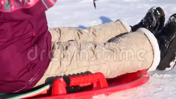 冬天散步的孩子一个女孩骑在塑料板上的雪滑板上视频的预览图