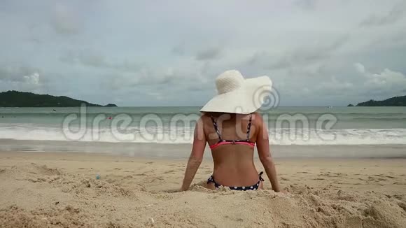 可爱的女人穿着白色宽边躺在阳光明媚的沙滩上视频的预览图